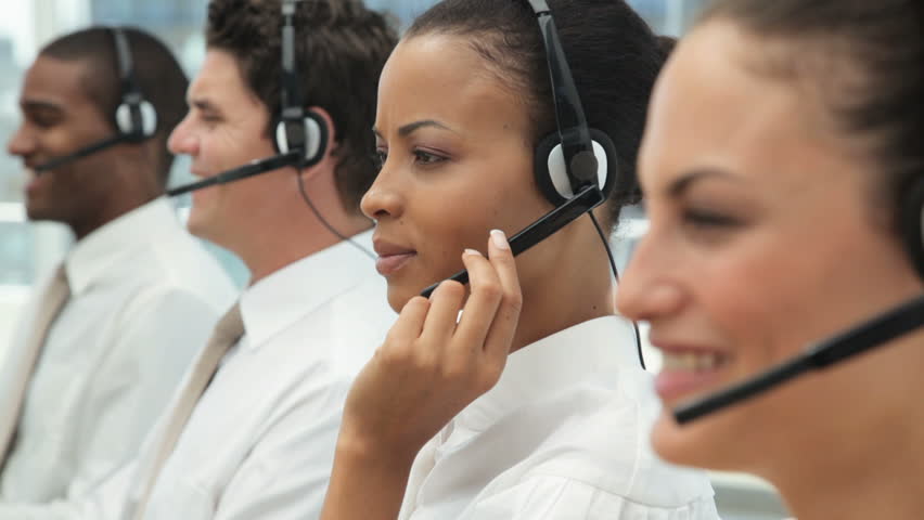 Young businesspeople talking on headsets. One attractive businesswoman turns towards the camera and smiles.