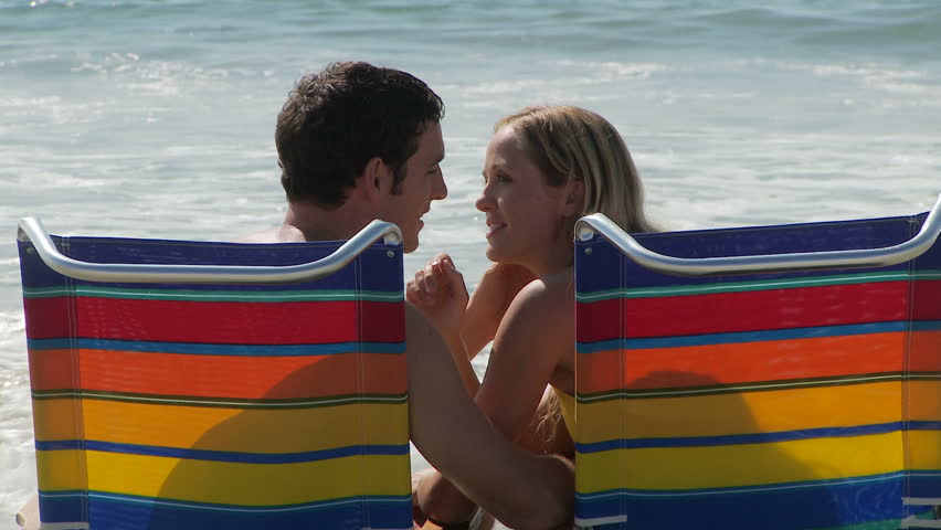 Close up of young couple sitting in lounge chairs by ocean and kissing