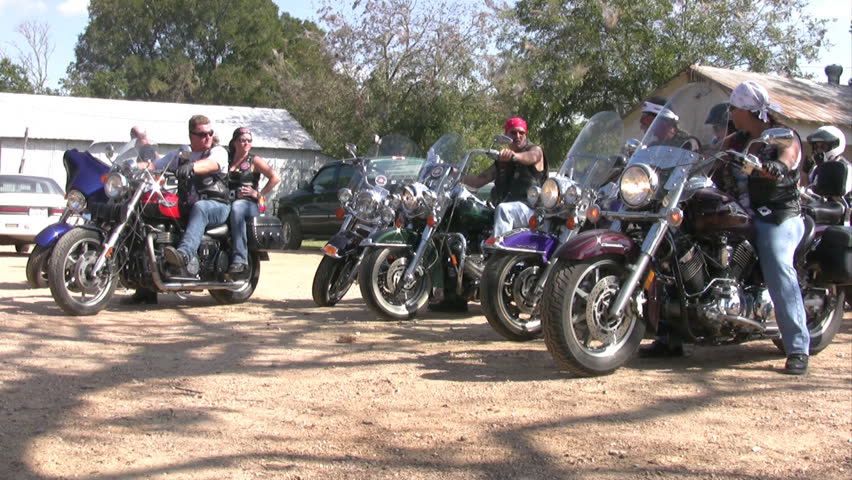 Video of motorcycles leaving Luckenbach Texas. Large group of motorcycle riders with Harley. Large oak trees and small country store and environment. 