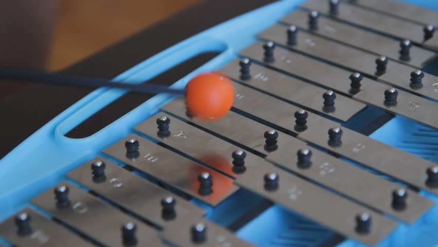 Glockenspiel. Playing a blue children's glockenspiel with an orange rubber mallet. Closeup and shallow DOF. 