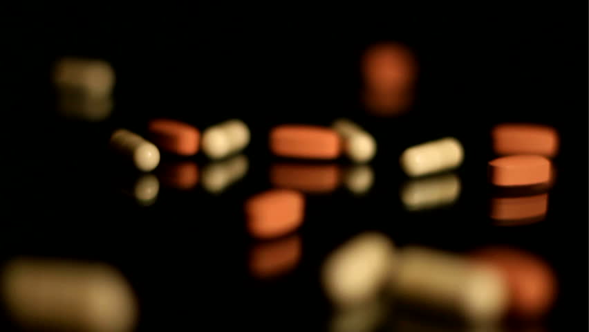 Pills capsules falling onto black glass, slow motion