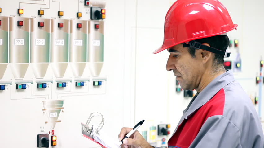 Engineer standing in front of the control panel in the control room and write the results of the measurements.