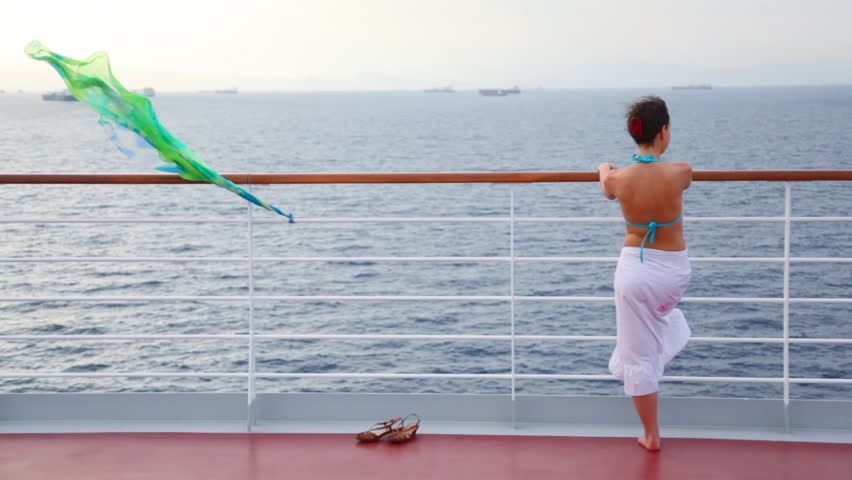 young woman stands on deck of cruise liner and looks at sea