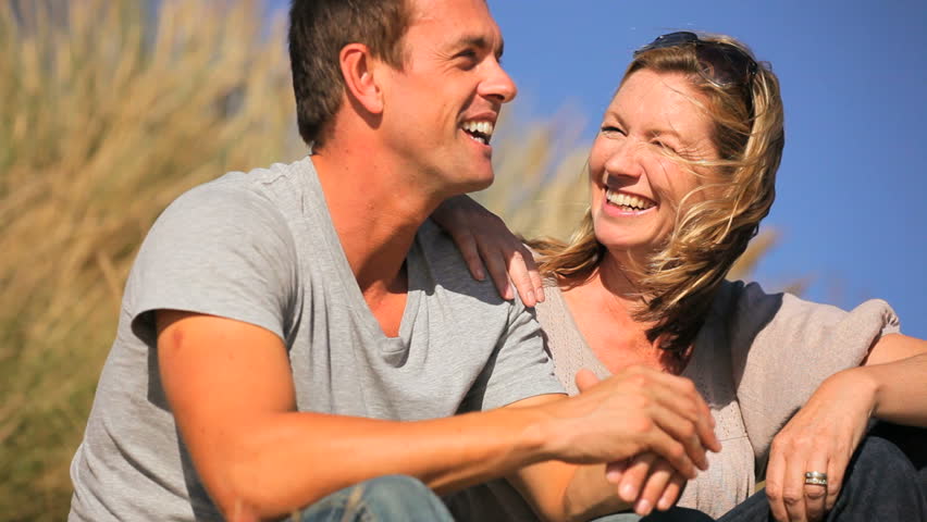 Attractive young caucasian couple enjoying quiet time together sitting in sand dunes at the coast