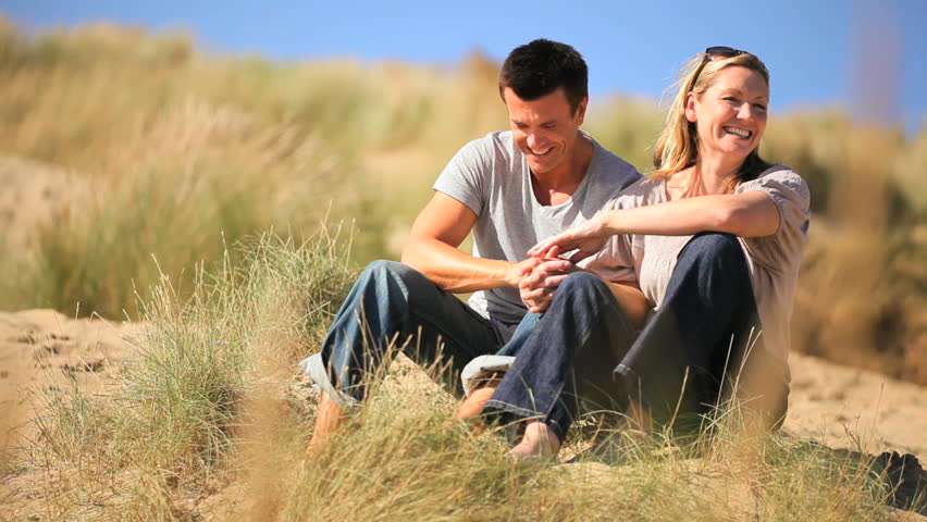 Attractive young caucasian couple enjoying quiet time together sitting in sand dunes at the coast