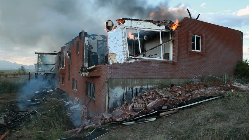 Fire burns a brick and wood house as firefighters let it finish burning. Brick collapse as structure is weakened and roof has completely burned. Fire and smoke coming from many windows and openings.