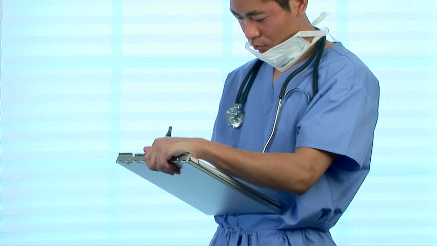 Young Asian doctor filling out medical chart in scrubs