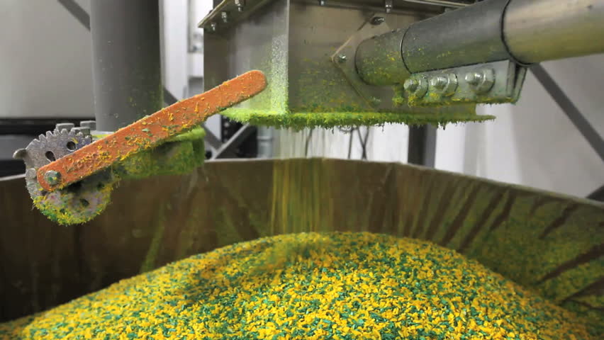 Bright yellow and green plastic pellets pour from a machine 