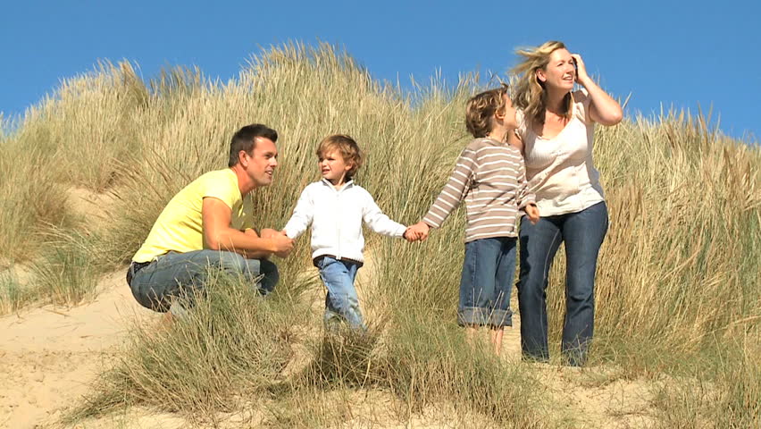 Attractive young caucasian family enjoying leisure time together on coastal sand dunes  filmed at 60FPS
