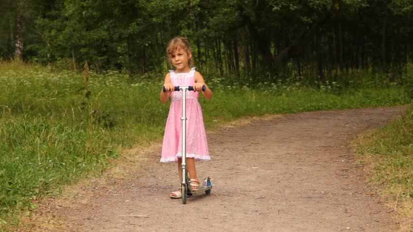 girl is riding a scooter merrily along the park road on a summer morning. 