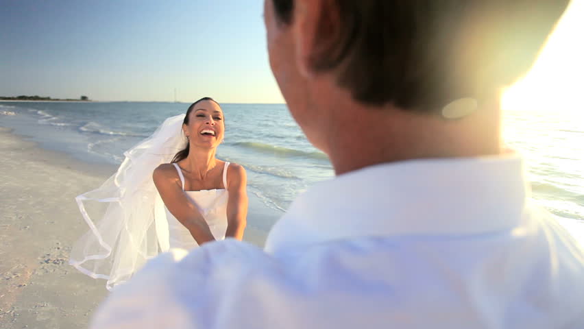 Attractive couple celebrate their wedding on a beautiful sandy beach as the sun goes down