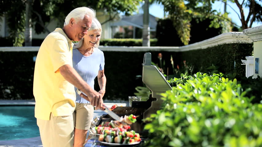 Senior couple enjoying healthy eating grilling food on a barbecue outdoors