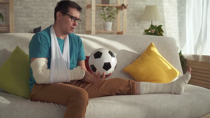 Portrait Sad Injured Athlete Sitting On The Couch With A Soccer Ball