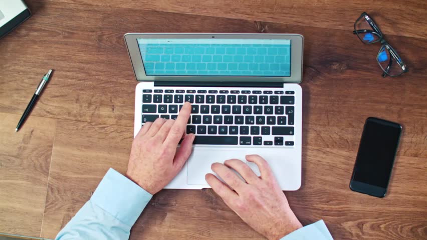 Desk Top View businessman typing on his laptop on a wooden desk table. top view Desk Top View businessman typing on his laptop on a wooden desk table. top view