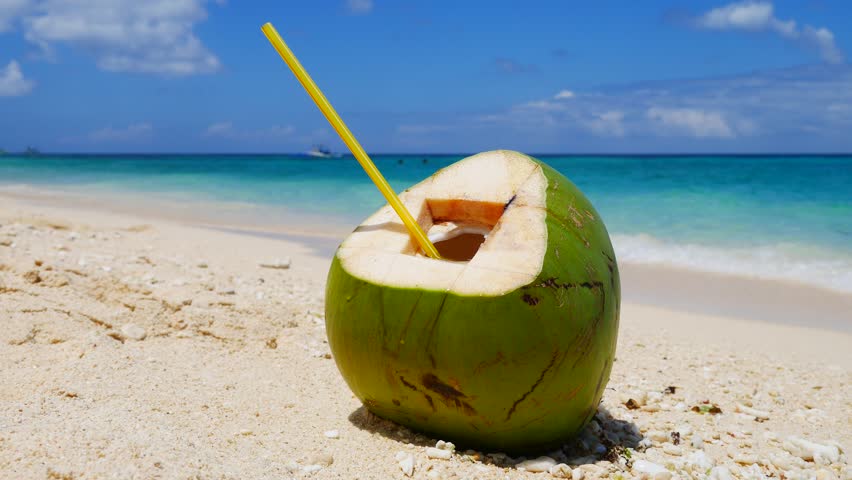 Green Coconut Served With Straw And Flower Decoration On Beach Towel To