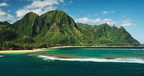 Aerial view flying over tropical coral reef lagoon towards beautiful green mountains on Kauai
