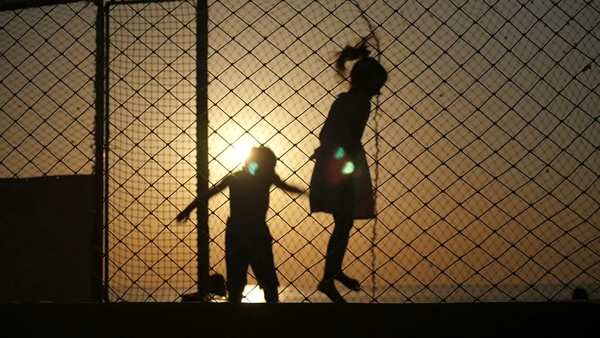 silhouettes of boy and girl jumping on the trampoline on a background of ocean sunset backlit