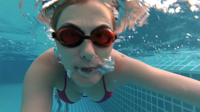 Underwater View As Woman Swims Towards Camera And Waves As She Blows