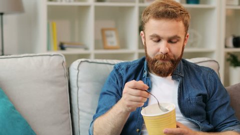 Portrait of young man who eating ice cream while relaxing on sofa in the living room at home.