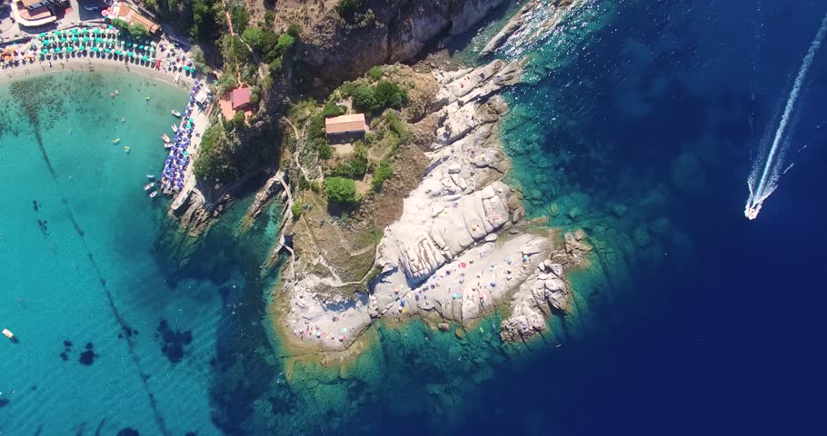 A speedboat circles through the sea around a picturesquare peninsula on a warm sunny day