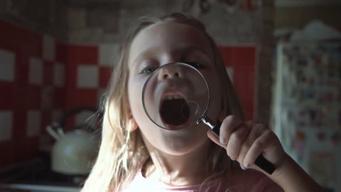 Toddler Cum Porn - Smiling little girl playing and grimacing with magnifier on kitchen.