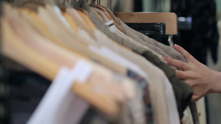 Woman's hands run across a rack of clothes, browsing in a boutique. Head-on view