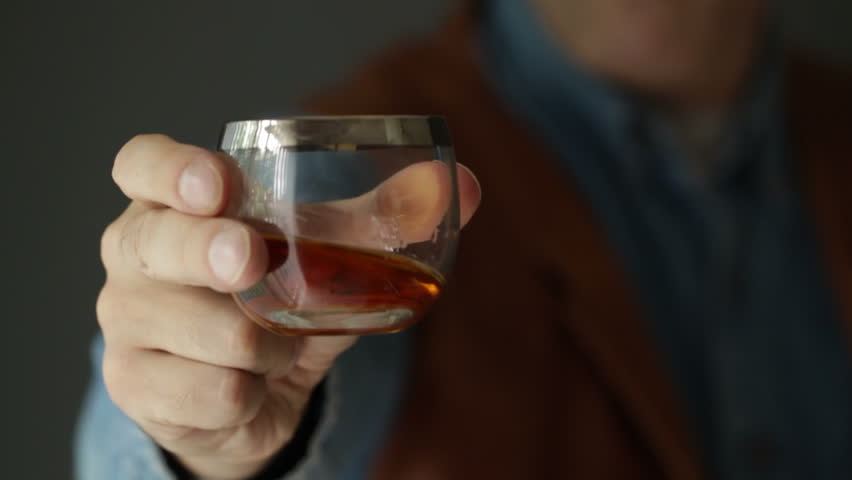 Hand Holding A Glass Of Whiskey On The Rock In Bar. Man Shake Alcohol 