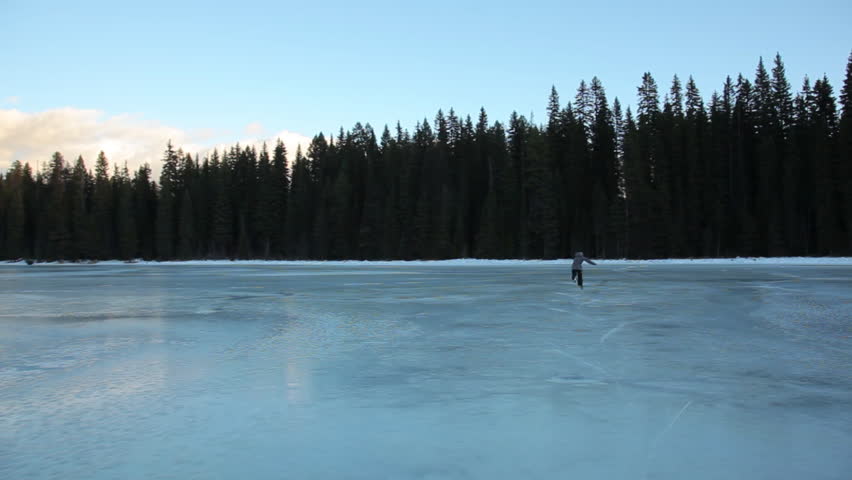 Man Ice Skating On A Frozen Lake With Forest In The Background