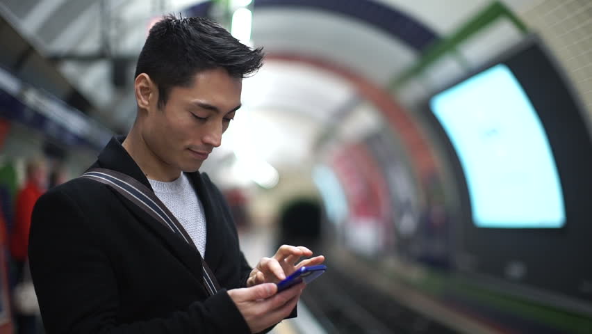 Young Asian Man Using His Phone In A Subway Station As His 